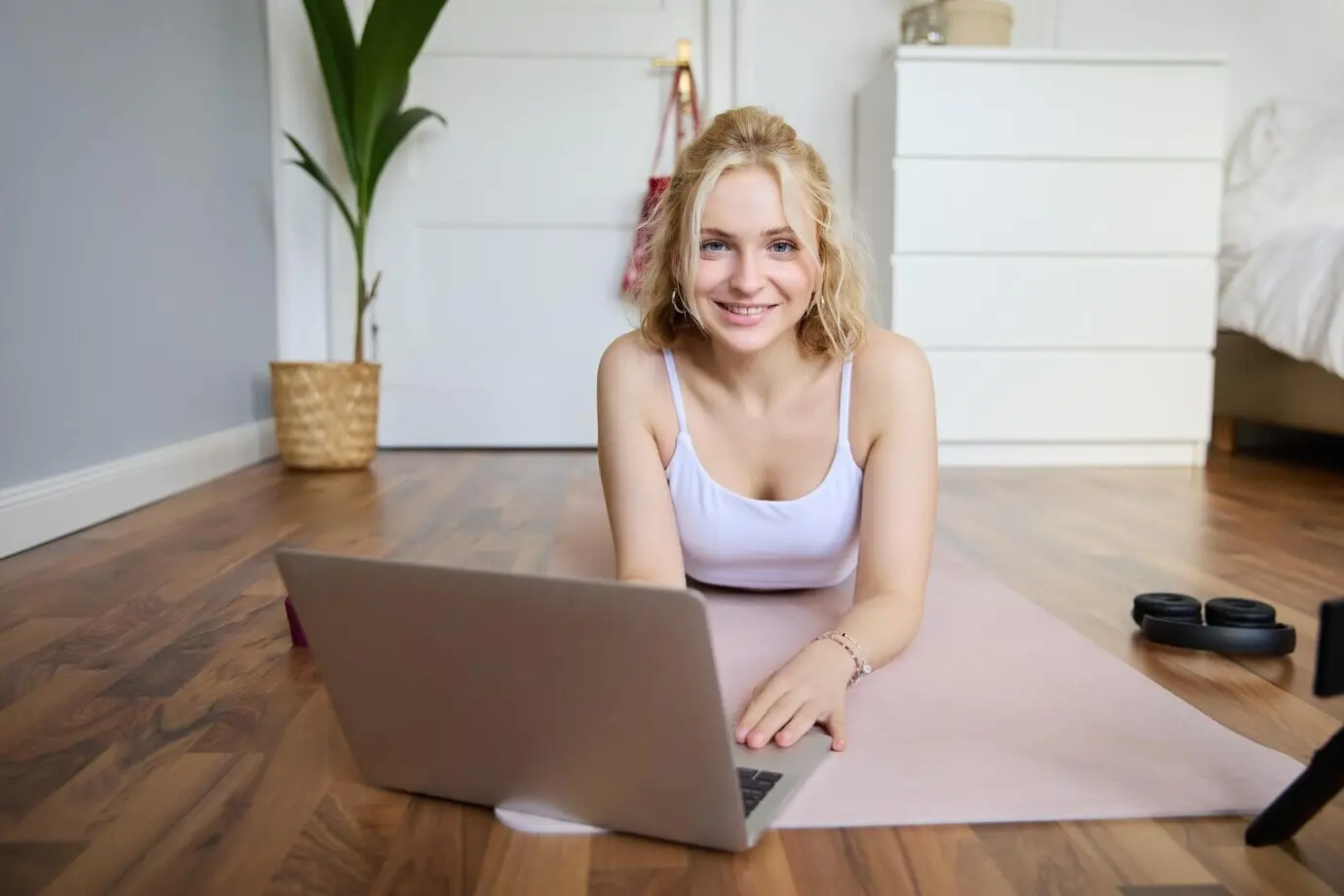 Porträt einer schönen blonden Frau, die auf einem Laptop Fitness-Videotutorials anschaut, während sie auf einer Gummi-Yogamatte liegt.